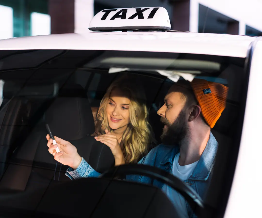 En mand sidder på førersædet i en taxa og viser noget til en kvinde på bagsædet på en oversætter, som han holder i hånden. Kvinden smiler interesseret. Et taxiskilt er synligt på taget af bilen.