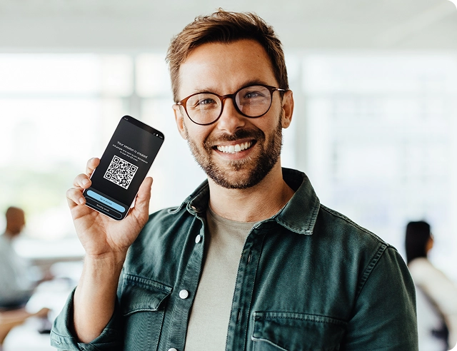 En smilende mand, der holder en smartphone med en QR-kode til tilmelding til Vasco Audience.